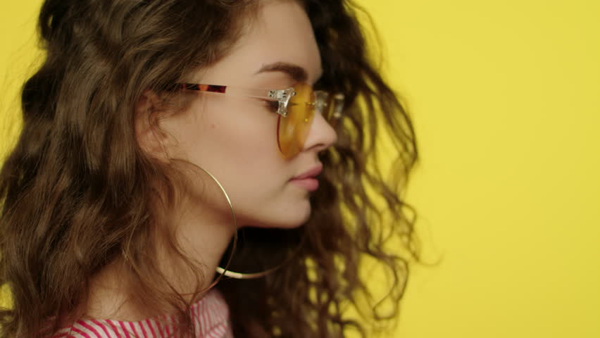 Playful woman in yellow glasses looking to camera. Portrait of fashion girl winking eye in studio. Close up of young woman in sunglasses winking to camera on yellow background. Fashion model wink eye Royalty-Free Stock Footage #1026902267