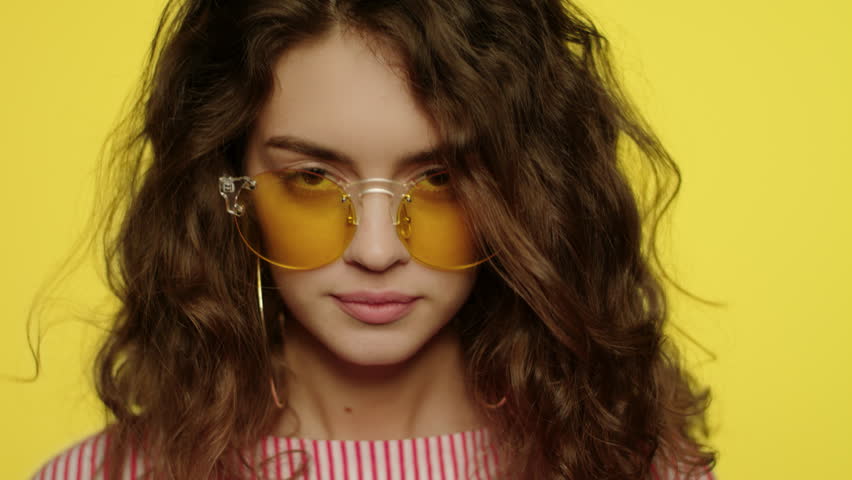 Young woman smiling on yellow background. Portrait of happy girl smiling in studio. Close up of fashion model smile. Happy woman in yellow sunglasses looking in camera | Shutterstock HD Video #1026902270