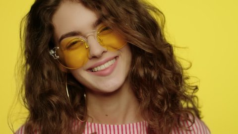Young woman smiling on yellow background. Portrait of happy girl smiling in studio. Close up of fashion model smile. Happy woman in yellow sunglasses looking in camera