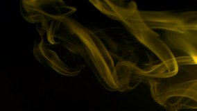 Slow motion, Vertical video: Trickle yellow smoke slowly rising graceful twists up on black background. Cigar smoke blowing from the right side. Closeup, isolated on black background.