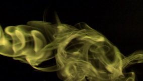 Vertical video: Thin trickle bright yellow smoke slowly rising graceful twists up on black background. Cigar smoke blowing from the left side. Closeup, isolated on black background.