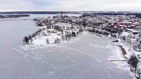 Drone footage flying towards the small town of Strängnäs with a beautiful windmill a great old cathedral. Flying over a frozen lake with some jetties. Filmed in realtime at 4k.