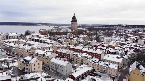 Drone footage flying over a small town towards the great old cathedral of Strängnäs. Colorful houses underneath and a frozen lake in the background.