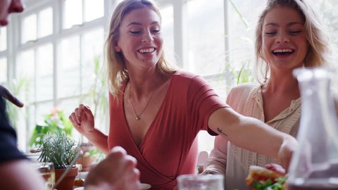 Two young adult white women eating lunch with friends at a restaurant, low angle