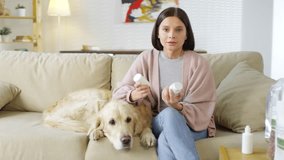 Medium shot of female dog owner sitting on couch with her Golden retriever and asking vet questions about medicines