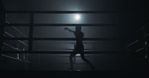 Female boxer training in the dark ring. Slow motion. Silhouette. Boxing concept