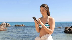 Surprised woman in bikini reading smart phone content on the beach on summer vacation