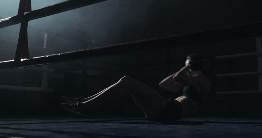 Young woman doing abdominal exercise in the boxing ring. Girl training, silhouette