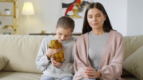 Medium shot of Caucasian woman with her young daughter holding red guinea pig sitting on sofa and talking with veterinarian by video link