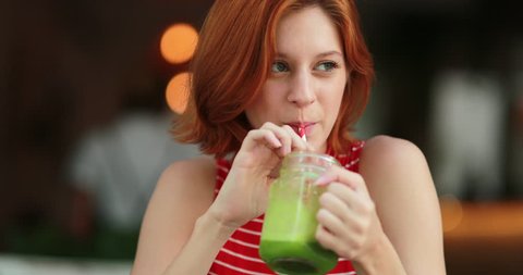 Pretty girl drinking green juice. Redhair young woman holding detox drink smiling and laughing