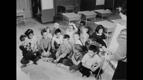 CIRCA 1960s - Students participate in an oral composition program and their teacher uses a whiteboard in an elementary school classroom.