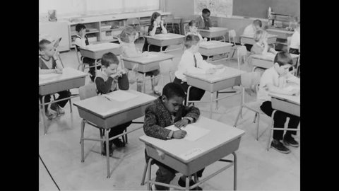 CIRCA 1960s - A teacher reads sentences and students circle words in their workbooks in a classroom in an elementary school.