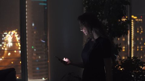 businesswoman walking in a dark office with a smartphone in her hands. portrait of a girl at the workplace on the background of the night city.