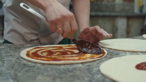 Cook spreading tomato sauce on pizza dough