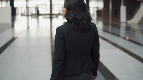A business woman exits through the revolving doors of a modern business center. girl in a business suit looks at watch. back view