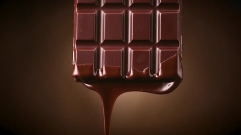 Chocolate bar with melted dark chocolate dripping over dark brown background. Confectionery concept backdrop. Melted premium chocolate flowing. Sweet dessert. 4K UHD video, slow motion