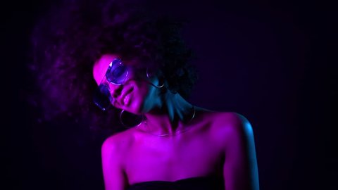 Tempting woman with perfect make-up smiling, enjoying moment, music. Young african girl with curly hair dancing in neon light. Glamour, fashion, style concept.