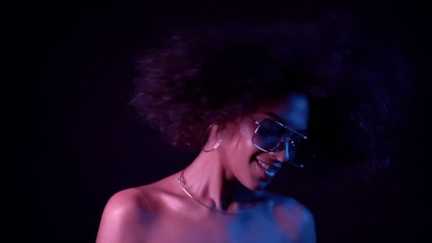 Young african girl with curly hair dancing in neon light. Tempting woman with perfect make-up smiling, enjoying moment, music. Glamour, fashion, style concept