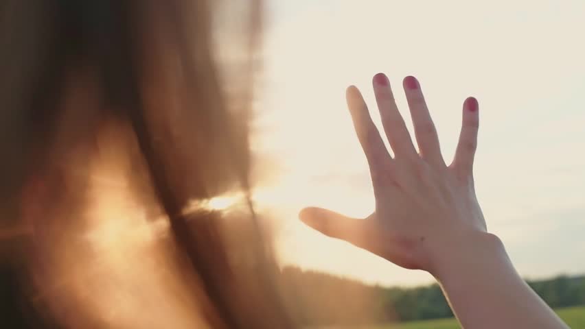 Close-up of a female hand, the sun is shining through the fingers. The sun's rays shine through the fingers of a girl at sunset. | Shutterstock HD Video #1026947426