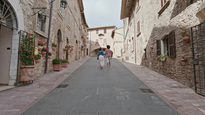 Romantic couple walking visiting rural town of Assisi.Back follow.Friends italian trip in Umbria.4k slow motion