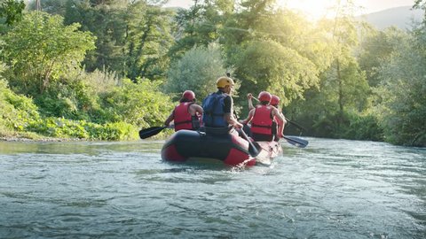 Group of people on raft boat doing rafting on river during sunset or sunrise. Warm back light. Friends italian trip in Umbria. 4k slow motion