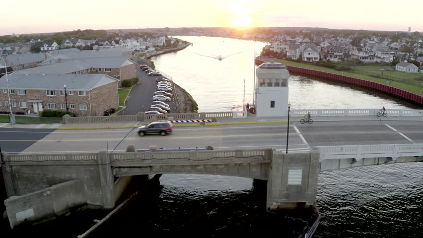 Aerial drone shot over a bridge and a river heading out into the Atlantic Ocean through the city buildings of Belmar, New Jersey.