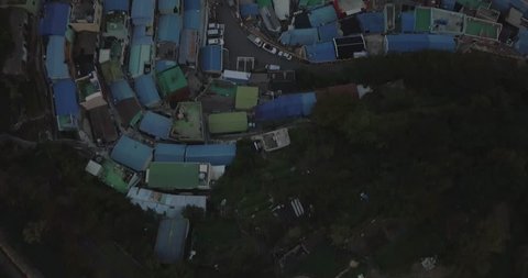 Drone looking down and then flying forward while panning up above a colorful city Gamcheon Culture Village below in Busan