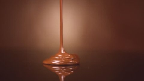 Chocolate pouring. Melted Liquid milk chocolate over brown background. Confectionery concept backdrop. Molten chocolate, sauce, topping. Sweet dessert. 4K UHD video, slow motion