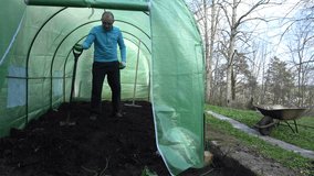 young man gardener work hard with shovel and dig compost in greenhouse. Static tripod shot. 4K UHD video clip.