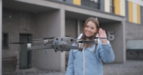 Female blogger waving hands at the camera. Attractive student taking selfie using copter. Beautiful woman looks at drone and takes selfie.