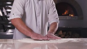 Hands prepare the dough on the background of fire. Chef preparing the pizza dough in slow motion on the background of the pizza oven. Food video.