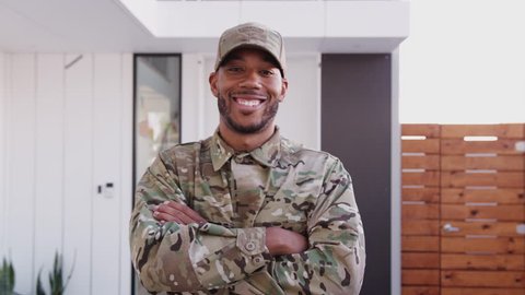 Millennial African American male soldier steps towards camera, crosses arms and smiles to camera, close up