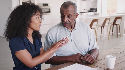 African American female healthcare worker showing a senior man how to use an assistance alarm during a home visit