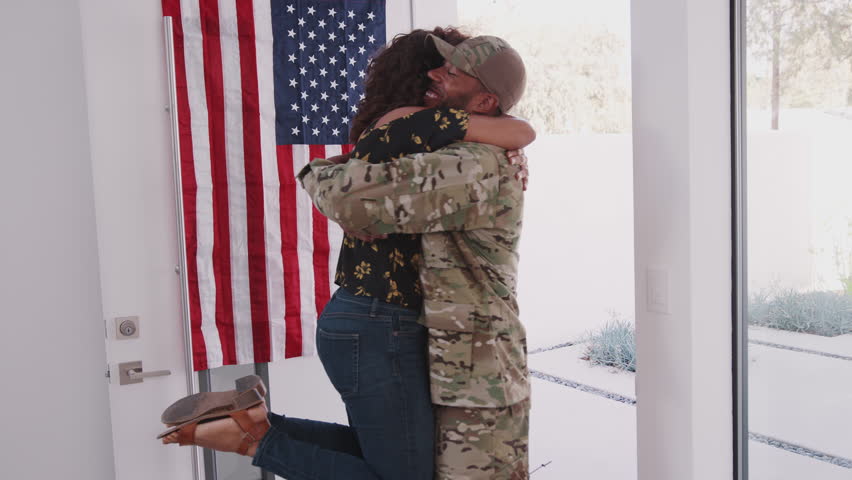Young African American woman running to the front door and welcoming home her soldier husband