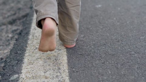 Close up of child legs walking away on road. Children without shoes are walking barefoot.