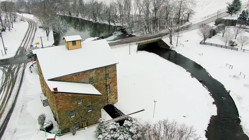 Mascot Roller Mills, Ressler mill Pennsylvania from the air, slow dolly shot of vintage three-story stone building with a small stream in the background, winter time, snow-covered landscape