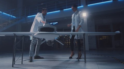 Meeting of Aerospace Engineers Working On Unmanned Aerial Vehicle / Drone Prototype. Aviation Scientists in White Coats Talking. Commercial Aerial Surveillance Aircraft in Industrial Laboratory