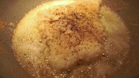 Halibut fish cooking with yellow butter in a pan.