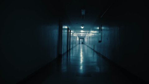 Tracking inside a long dark gloomy corridor, tunnel past the small windows to the old ajar doors with glass inserts. Concept of horror.