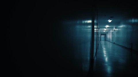 Tracking inside a long dark gloomy corridor, tunnel past the small windows to the old open doors with glass inserts. Concept of horror.