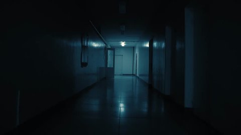 Tracking inside a long dark gloomy corridor, tunnel. On the wall at the end of the path there is a white big clock, it shows a quarter to eleven. Concept of horror.