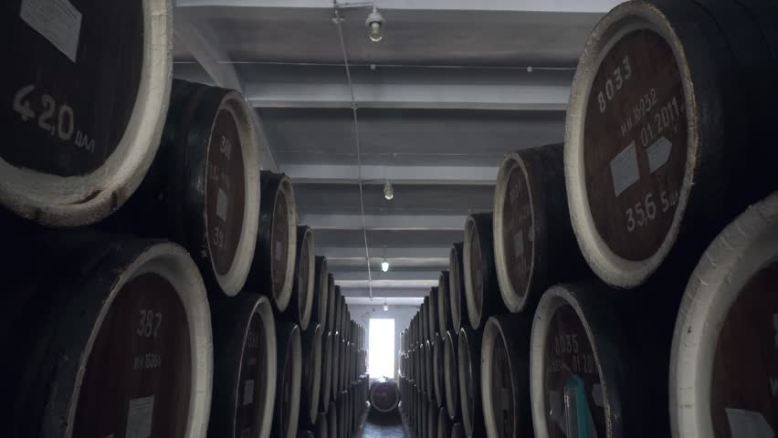 Barrels of cognac, wine or whiskey. Extract of brandy in oak barrels. Alcohol warehouse. Hundreds of barrels in an underground vault. Camera movement between barrels.