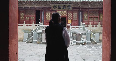 Asian master of Tai chi martial arts from behind, looking at temple in Wudang China. Slow motion, red cinema camera. Note: Chinese symbols, Taoism, practice has a purpose don't forget core belief.