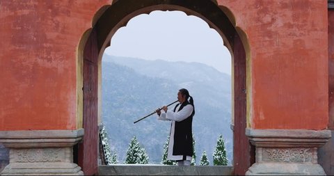 Asian master, demonstrates blowing Chinese bamboo flute in Wudang mountain China. Slow motion, red cinema camera,  hand held. 