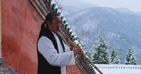 Asian master, demonstrates blowing Chinese bamboo flute in Wudang mountain China. Slow motion, red cinema camera,  hand held. 