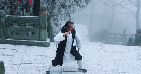 Asian master, demonstrates Tai chi martial arts sword combat in Wudang mountain China. Slow motion, red cinema camera. 