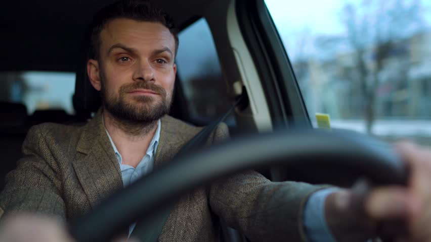 Satisfied bearded man driving a car down the street in sunny weather | Shutterstock HD Video #1027022357