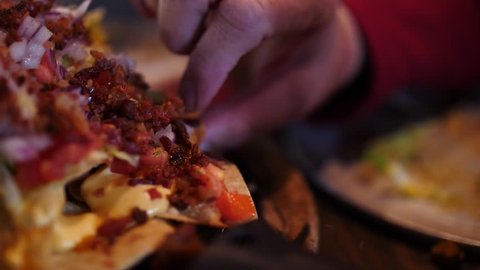 Close up on the hand of a person eating nachos helping themselves to a mouthful off a plate with their fingers