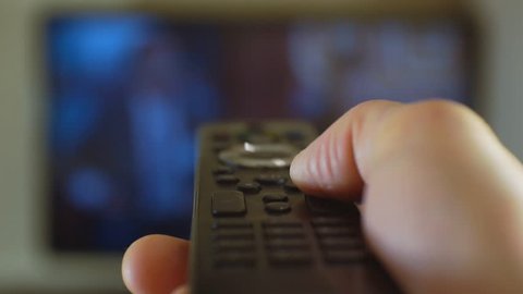 Hand turns off the TV by remote control. Remote control at the background of the screen TV panels. 