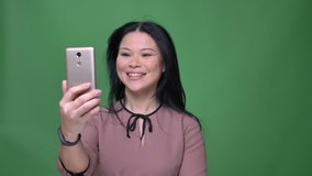 Closeup shoot of young attractive asian female with black hair having a video call on the phone with background isolated on green